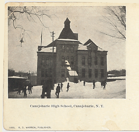 historic photo post card of a three story building made of stone. It is winter, children play out front in the snow. 